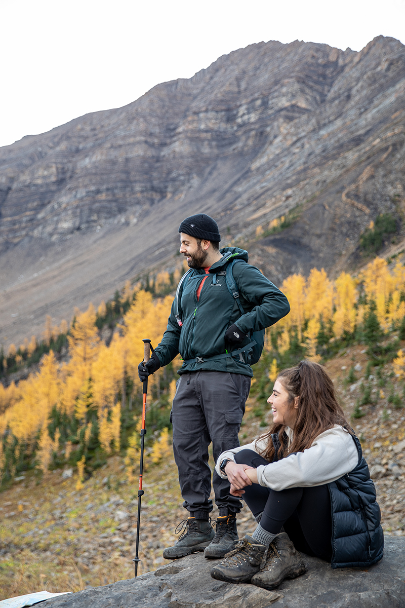 Two hikers taking a break while surrounded by mountains and yellow larch trees.