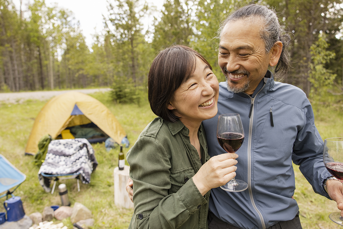 A couple by their campsite laughing and drinking wine.